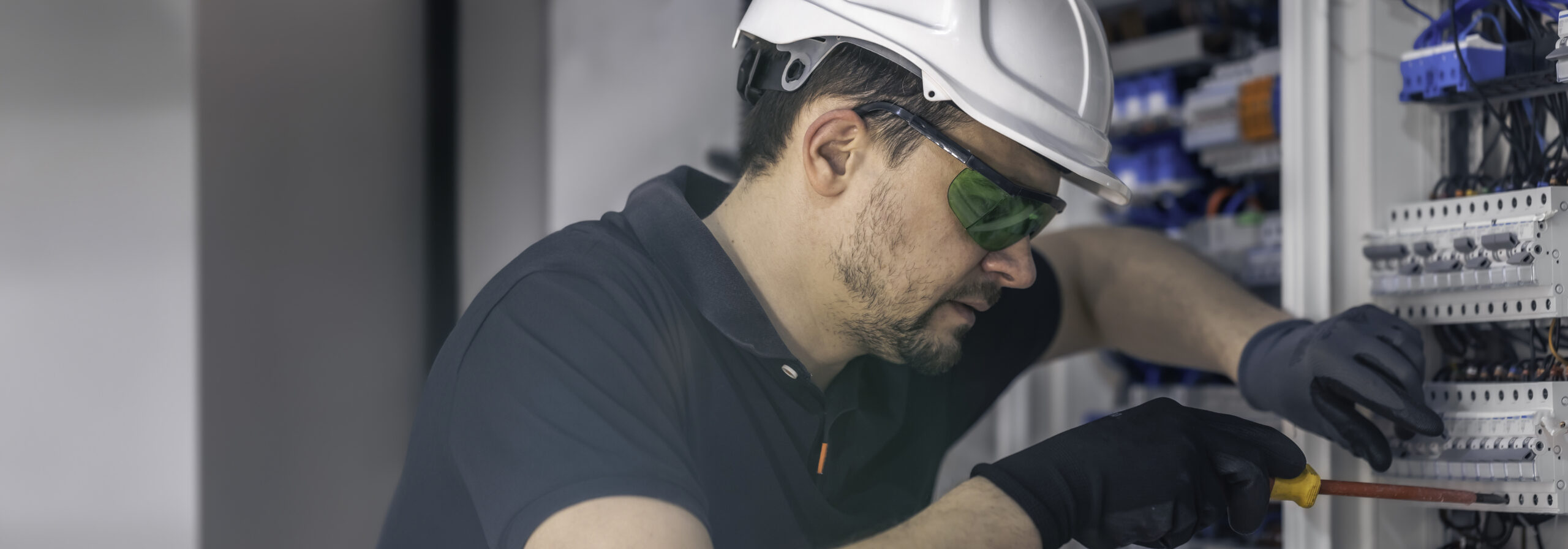 A male electrician works in a switchboard using an electrical connection cable.